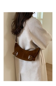 Close-up of brown suede crescent bag with metal buckles styled with a wool coat