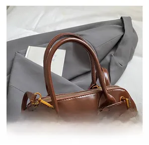 Detailed close-up of brown glossy shell bag with gold hardware and secure zipper closure