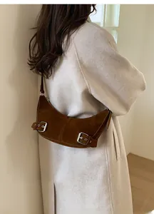 Vue latérale d'un sac d'épaule en daim marron foncé porté sur un fond minimaliste