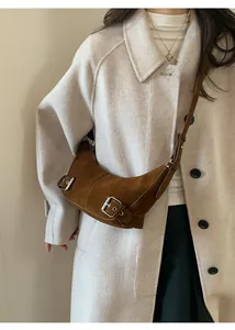 Détail d'un sac bandoulière en daim marron avec boucle argentée porté sur un manteau