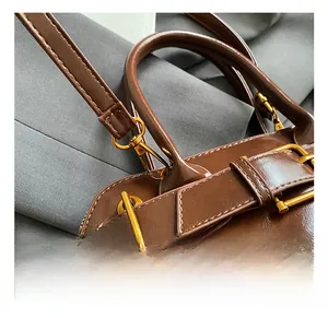 Close-up of golden metal hooks and decorative buckle straps on a brown leather handbag