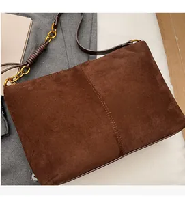 Detail of dark brown suede bag with vertical stitching and gold metal chain strap