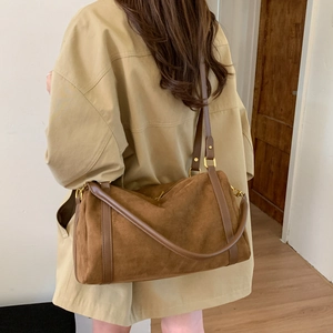 Détail du sac polochon en daim marron avec lanières en cuir et boucles en métal doré