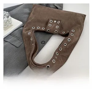 Détail d'un sac cabas en daim marron avec œillets métalliques et texture douce