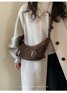 Détail d'un sac demi-lune marron foncé avec boucles argentées sur manteau