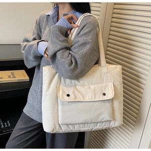 Detail view of off-white quilted tote bag with front pocket and dark metal buttons