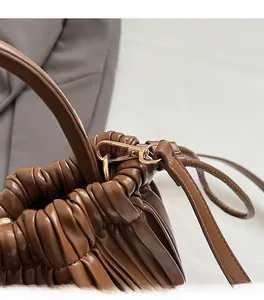Detailed close-up of premium gold hardware and elegant ruched pleats on a brown leather bag