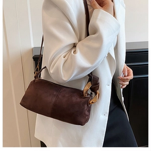 Close-up of deep brown suede handbag featuring a bold gold chain link and stitching