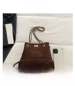Detail view of coffee suede bucket bag with long fringe and metal chain strap compared to phone