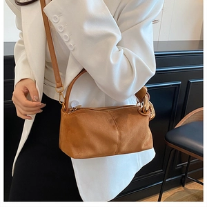 Detailed view of brown suede handbag featuring elegant gold metal hooks and soft texture
