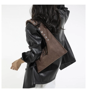 Detail of a brown suede shoulder bag featuring metallic silver grommets on a wide strap