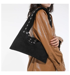 Close-up of black suede shoulder bag with silver eyelets and a wide strap on model