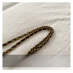 Detail of light gold metal chain strap woven with dark brown leather on white fabric