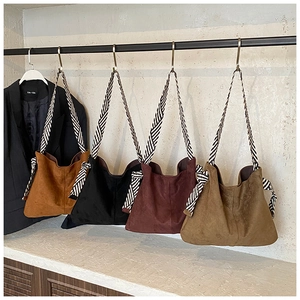 Detail of four matte suede tote bags in various colors with striped woven straps
