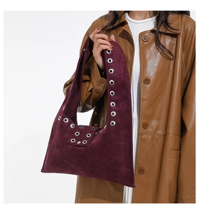 Détail du sac à bandoulière en daim bordeaux avec œillets métalliques et texture rustique