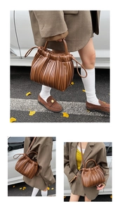 Detail of a brown pleated bucket bag with a fixed handle and detachable shoulder strap