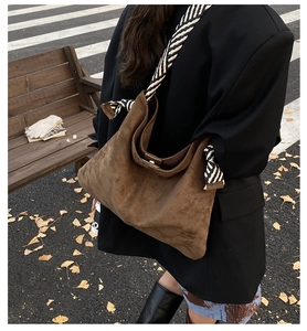 Detailed close-up of brown suede tote bag with striped woven strap in a street setting