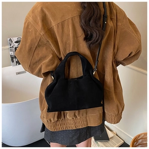 Rear view of a black suede dumpling handbag styled with a brown jacket in a minimalist room