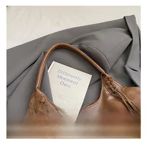 Sac hobo en cuir marron avec breloque à pompon tressé sur fond de veste de blazer grise
