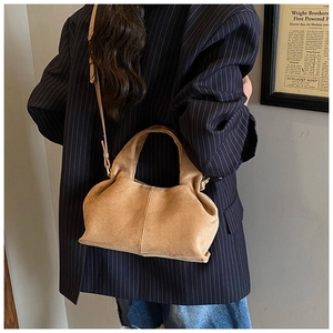 Detail of tan suede trapezoid handbag worn crossbody by a model in a minimalist urban setting