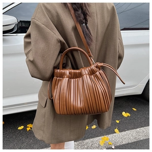 Detail of a brown pleated bucket bag with a cylindrical handle and leather texture