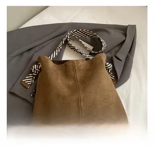 Detail of brown suede tote bag featuring a striped woven wide shoulder strap on grey blazer