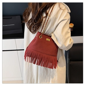 Detail of red quilted bucket bag with long tassels and gold chain strap on a trench coat