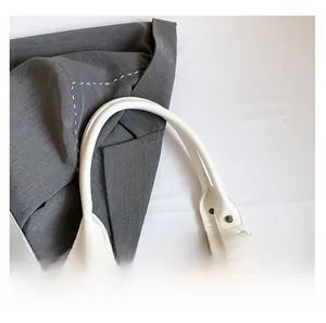Close-up of creamy white PU leather handbag featuring thick handles and vintage bronze rivets