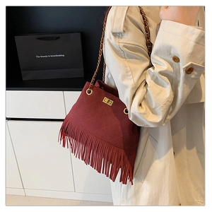 Detail of red suede tassel bucket bag with quilted patterns and golden chain strap