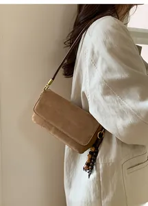 Brown suede crossbody bag detail featuring decorative wooden bead tassels and retro hardware