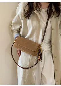 Detail of a brown suede shoulder bag with long wooden bead tassels and leather strap
