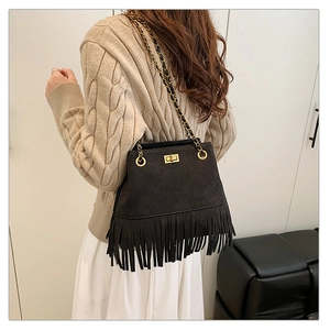 Detail of black quilted suede bucket bag with gold chain strap and long fringe decor