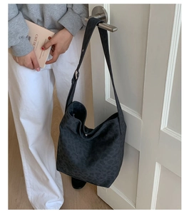 Detail of black leopard print crossbody bucket bag with adjustable wide strap on white door