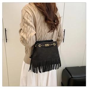 Detail of a black tassel bucket bag with gold chain strap on a knit sweater