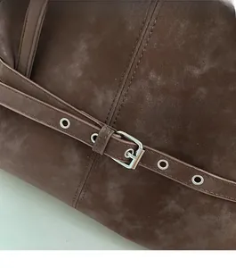 Detailed close-up of dark brown suede shoulder bag with silver buckle and eyelets