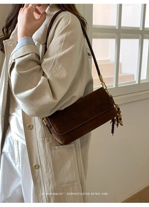 Close-up of dark brown suede shoulder bag with retro metal buckle and wooden bead tassel