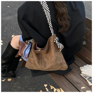 Close-up of large brown suede shoulder bag featuring a striped woven wide strap