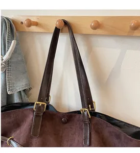 Detail of adjustable leather strap and golden metal buckle on a brown suede tote bag