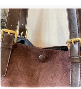 Close-up of brown suede tote bag featuring adjustable leather straps and magnetic closure