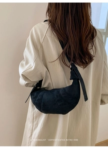 Close-up of minimalist black matte leather croissant bag worn on shoulder