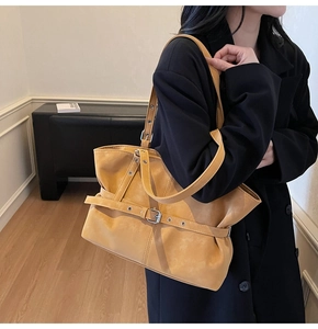 Detail of a mustard yellow faux leather tote bag with decorative buckle straps on black coat