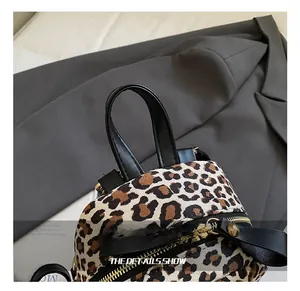 Close-up of leopard print backpack featuring black leather handle and gold hardware detail