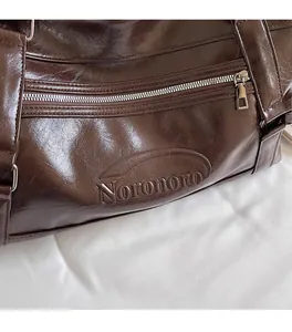 Detail of dark brown leather tote featuring brand logo and smooth oily texture surface