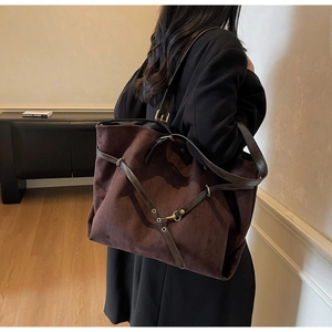 Detail of a large dark brown suede tote bag with double straps and metal buckle accents