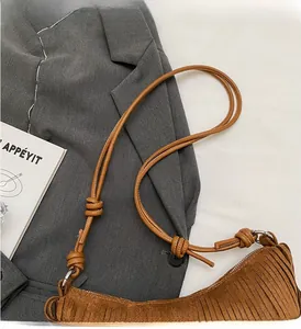 Detailed shot of brown suede crescent bag with fringe and knotted strap on gray blazer