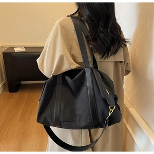 Detail of black canvas tote bag with leather straps on model wearing a trench coat