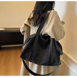 Detail view of large black canvas tote bag with leather straps and gold metal hardware