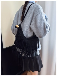 Detail of a black suede tassel crossbody bag featuring wooden bead strap accents