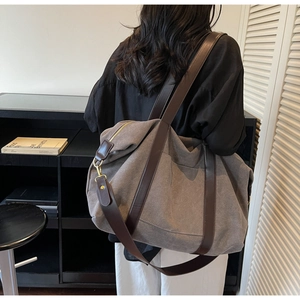 Close-up of a large grey canvas tote bag with brown leather straps and gold metal buckles