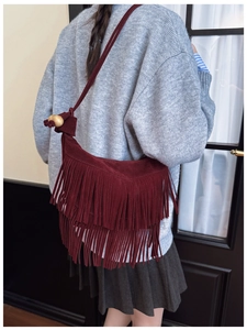 Detail of burgundy fringe crossbody bag with retro suede texture and decorative wooden beads